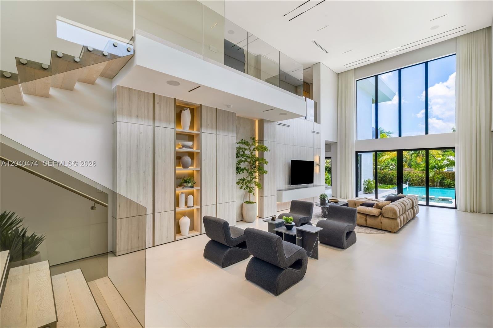 A modern, double-height living room features a floating staircase, light wood cabinetry, and floor-to-ceiling windows — 1008 NE 114th St, Biscayne Park FL 33161, BISCAYNE PARK, FL