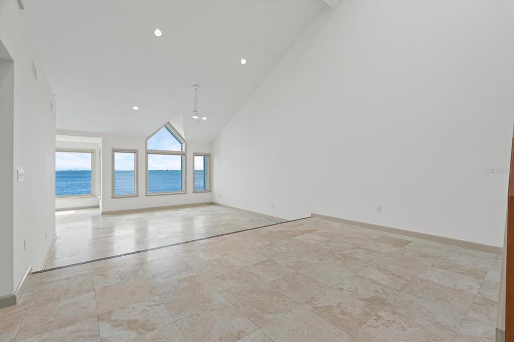 A spacious, white-walled room features vaulted ceilings, tile flooring, and large windows overlooking the ocean — 24 TIDY ISLAND BOULEVARD, BRADENTON, FL