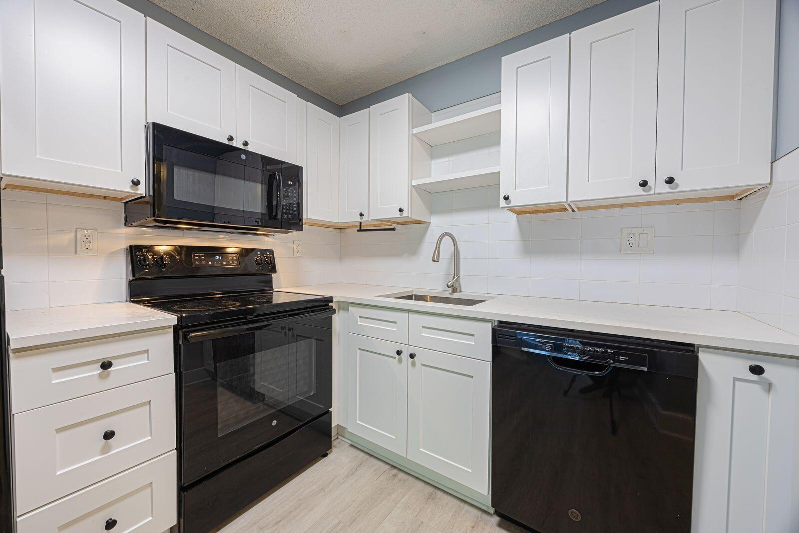 A kitchen features white cabinets, black appliances, a stainless steel sink, and white countertops — 9440 SW 8th Street # 417, Boca Raton FL 33428, BOCA RATON, FL
