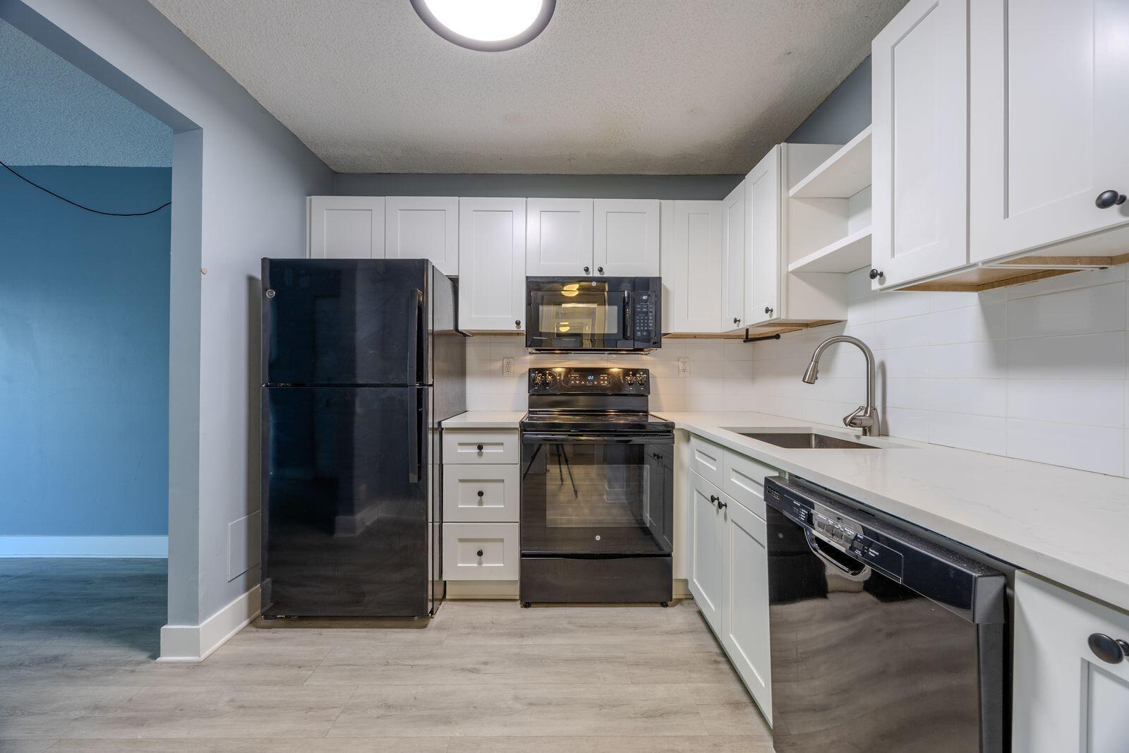 A kitchen features white cabinets, black appliances, a light countertop, and gray wood-look flooring — 9440 SW 8th Street # 417, Boca Raton FL 33428, BOCA RATON, FL