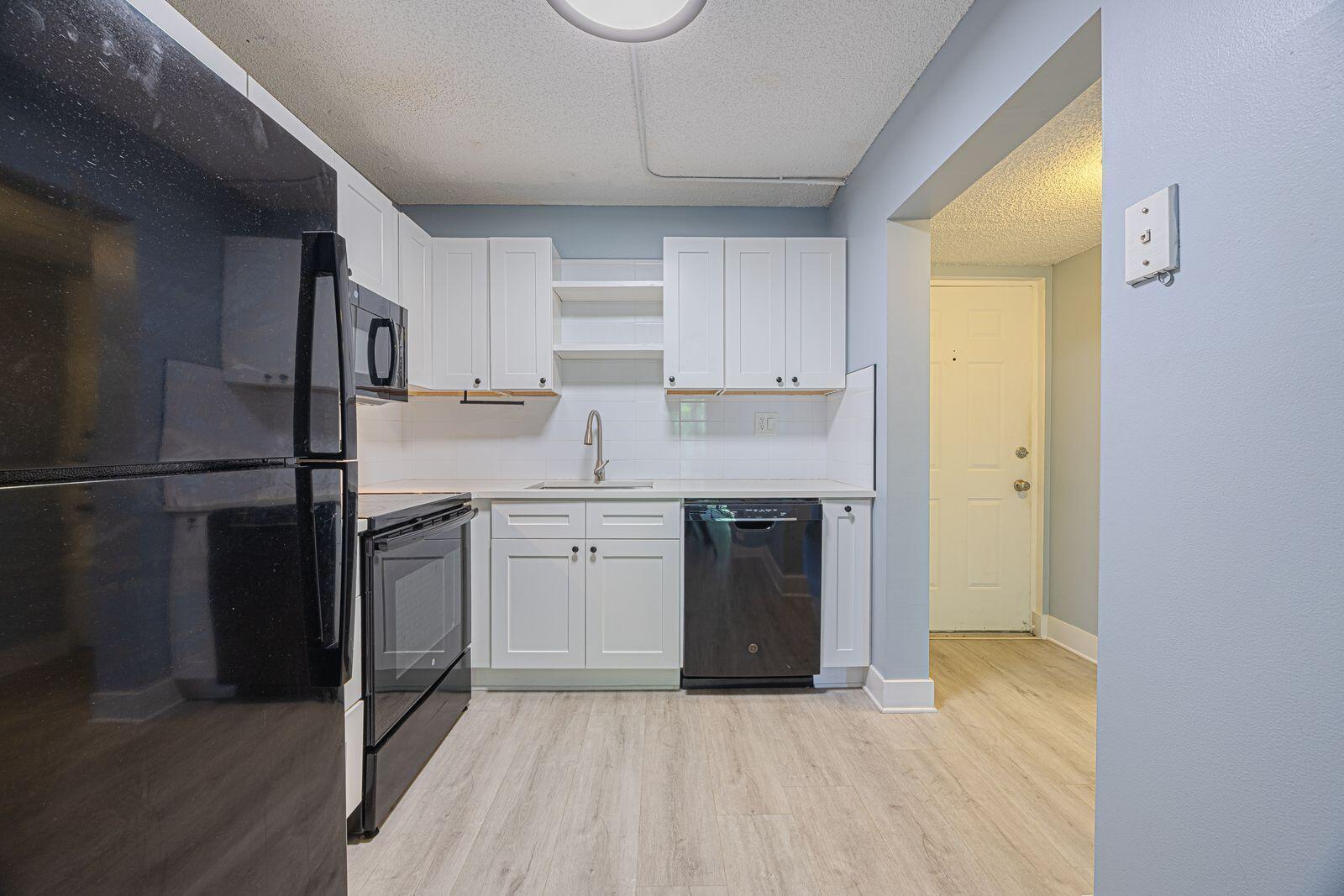 A kitchen features white cabinets, black appliances, a white tile backsplash, and light wood flooring — 9440 SW 8th Street # 417, Boca Raton FL 33428, BOCA RATON, FL