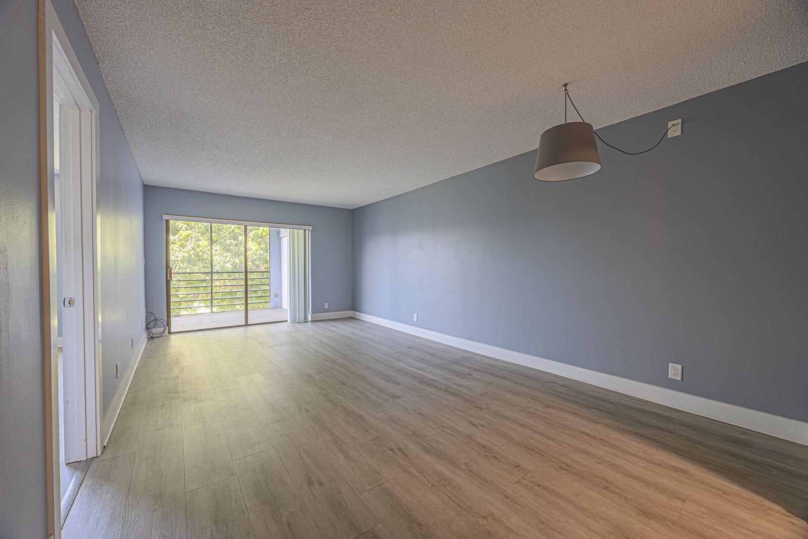 An empty living room features gray walls, wood-look flooring, a pendant light, and a sliding door — 9440 SW 8th Street # 417, Boca Raton FL 33428, BOCA RATON, FL