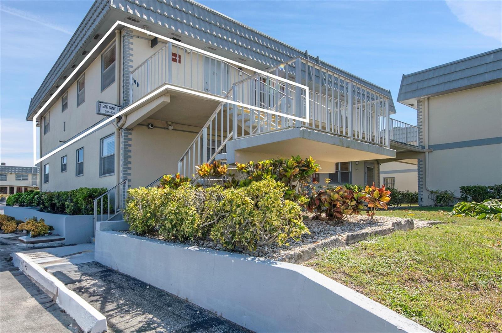 An exterior view of a two-story apartment building with a concrete staircase and metal railings — 409 Brittany I # 409, Delray Beach FL 33446, DELRAY BEACH, FL