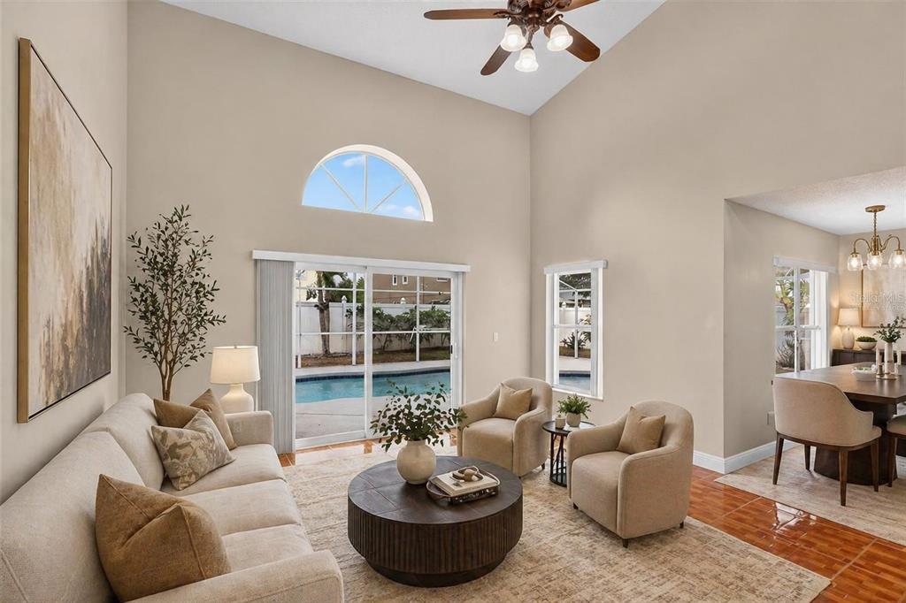 A living room with high ceilings, neutral furniture, a round coffee table, and a pool view — 14912 WHITE MAGNOLIA COURT, ORLANDO, FL