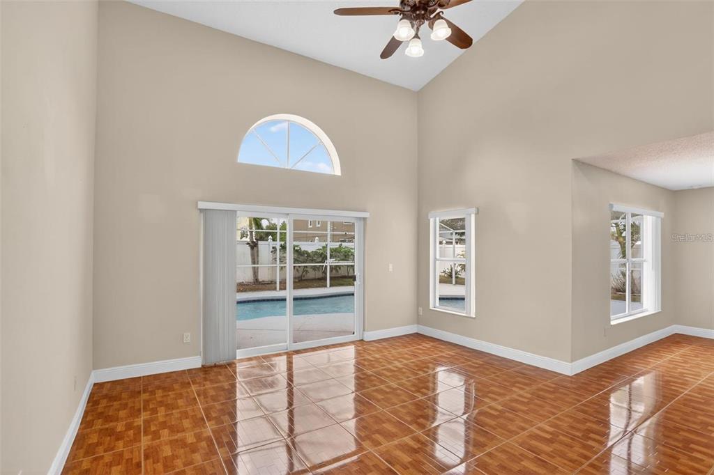 A bright living room with high ceilings, tile flooring, and sliding doors leading to a pool — 14912 WHITE MAGNOLIA COURT, ORLANDO, FL