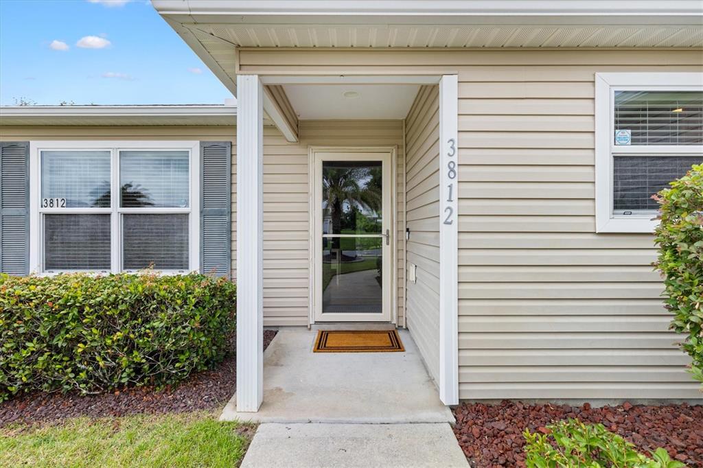 The exterior of a house features beige siding, a front door with a storm door, and windows — 3812 INFINITY RUN, THE VILLAGES, FL
