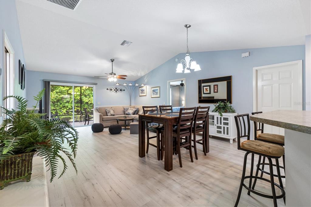 A bright open-concept living and dining area features light wood flooring and vaulted ceilings — 3812 INFINITY RUN, THE VILLAGES, FL