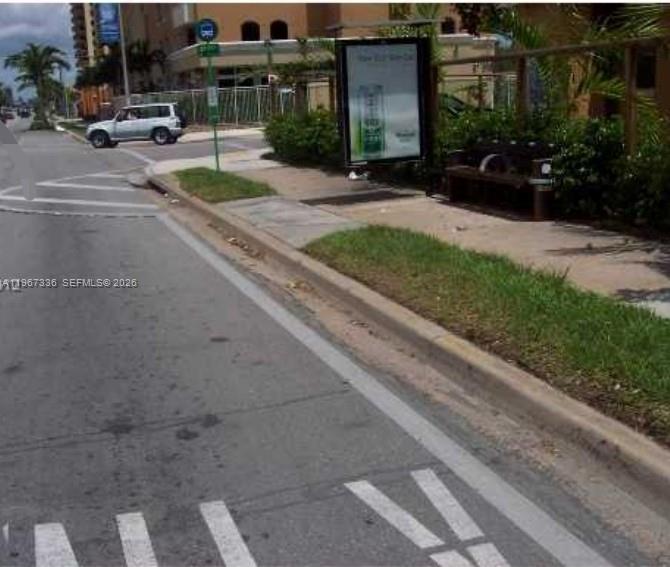 A street-level view shows a bus stop with a bench and advertisement sign near road — 2441 SW 27th Ave, Miami FL 33145, MIAMI, FL