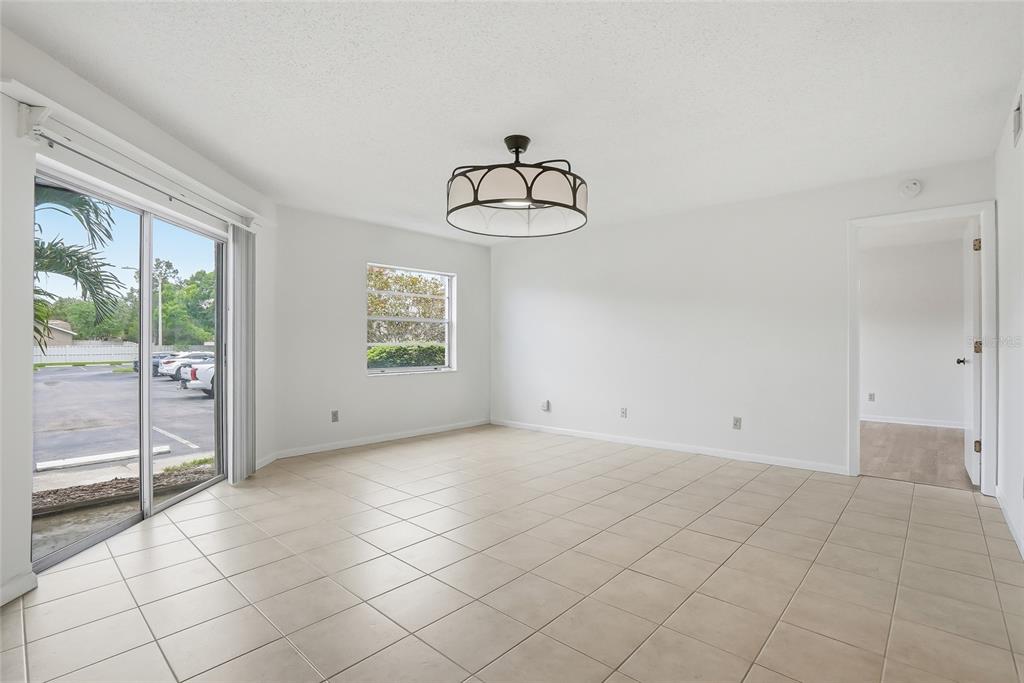 A bright, empty dining room features white walls, tile flooring, a chandelier, and sliding glass doors — 500 SANTA CRUZ PLACE NE UNIT D, ST PETERSBURG, FL
