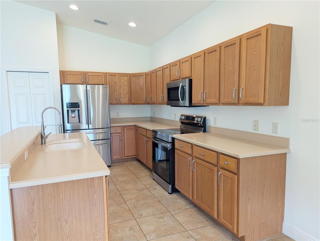 A kitchen features oak cabinets, stainless steel appliances, and light-colored countertops over tile flooring — 1882 W ANGELICA LOOP, LECANTO, FL