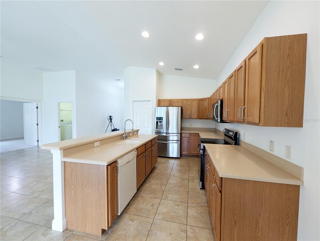 A kitchen features oak cabinets, tan countertops, stainless steel appliances, and tile flooring — 1882 W ANGELICA LOOP, LECANTO, FL