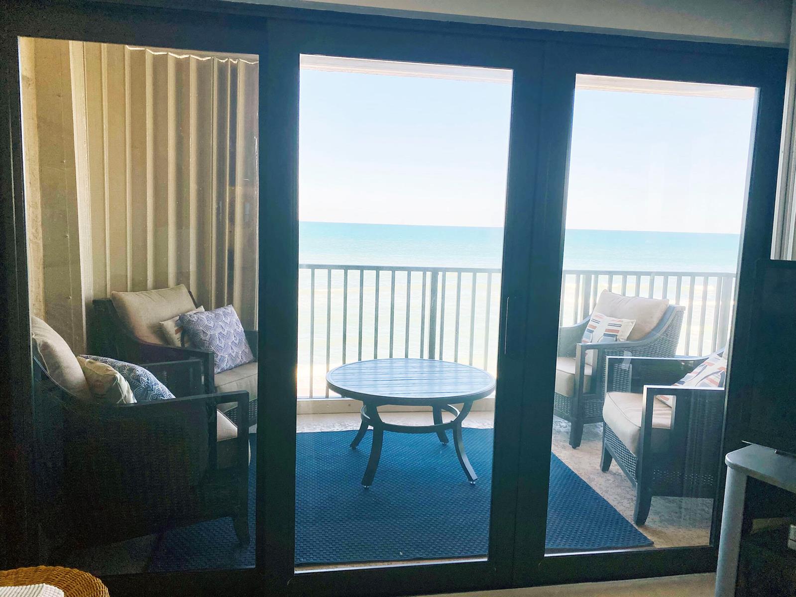 A balcony with four chairs and a round table overlooks the ocean through sliding doors — 10200 S Ocean Drive # 710, Jensen Beach FL 34957, JENSEN BEACH, FL