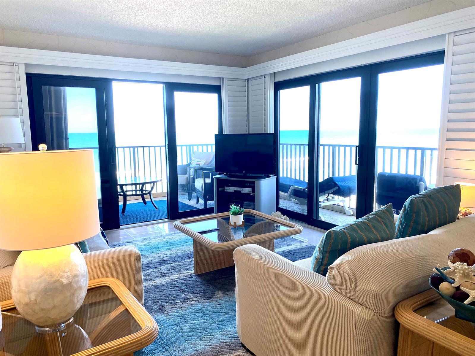 A living room features a beige sofa, glass coffee table, and sliding doors overlooking the ocean — 10200 S Ocean Drive # 710, Jensen Beach FL 34957, JENSEN BEACH, FL