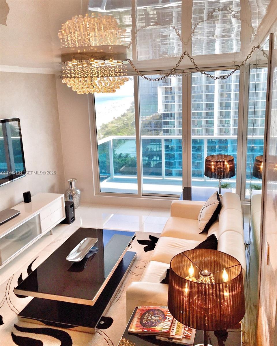A modern living room features a white sofa, black coffee table, crystal chandelier, and balcony view — 2301 Collins Ave # 1507, Miami Beach FL 33139, MIAMI BEACH, FL