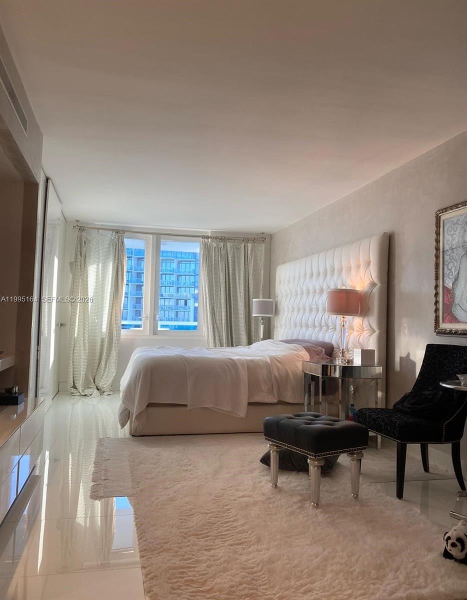 A bedroom features a tufted white headboard, white tile flooring, and a large window — 2301 Collins Ave # 1507, Miami Beach FL 33139, MIAMI BEACH, FL