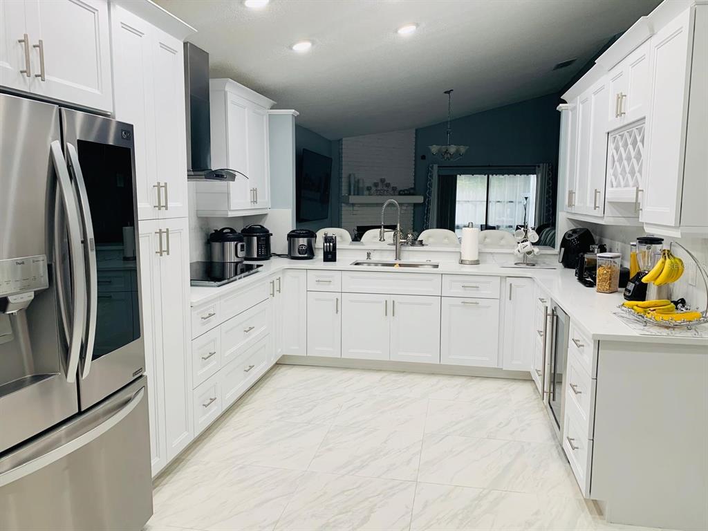 A modern white kitchen features stainless steel appliances, marble-look tile flooring, and quartz countertops — 2062 SUE ELLEN COURT, APOPKA, FL