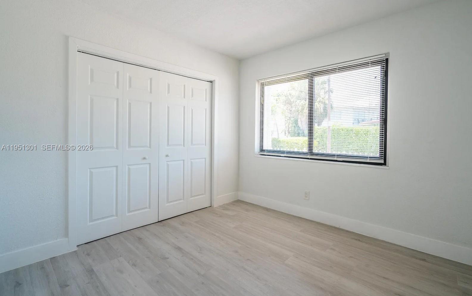 A bedroom with white walls, light wood-look flooring, and multiple white paneled closet doors — 1248 Marseille Dr # 2, Miami Beach FL 33141, MIAMI BEACH, FL