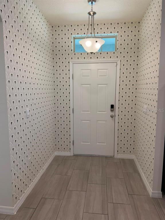 An entryway features patterned wallpaper, light wood-look tile flooring, and a central pendant light fixture — 17823 ADRIFT ROAD, WINTER GARDEN, FL