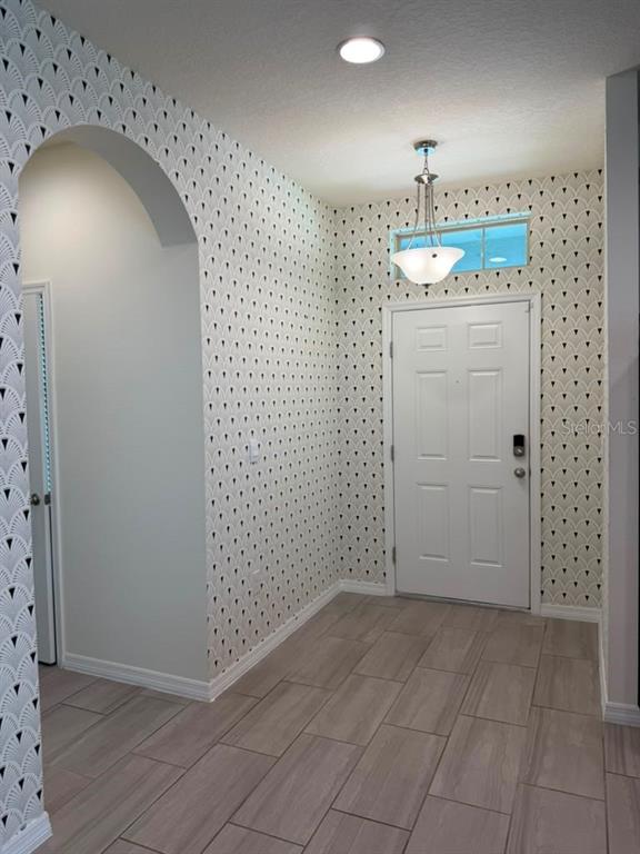 An entryway features patterned wallpaper, a white door, a pendant light, and light-colored tile flooring — 17823 ADRIFT ROAD, WINTER GARDEN, FL