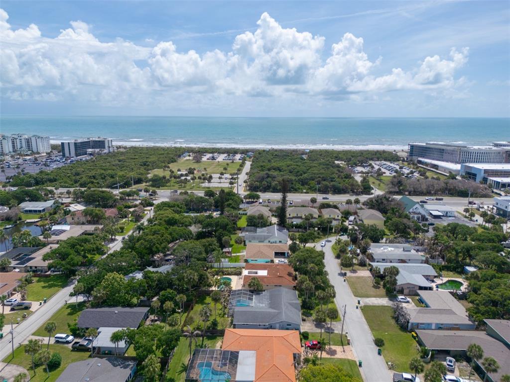 An aerial view shows a coastal neighborhood with houses, trees, and a beach in the distance — 124 JUNE DRIVE, COCOA BEACH, FL