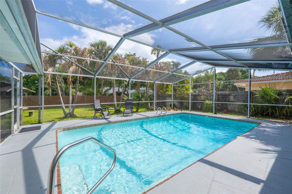 A swimming pool enclosed by a screened lanai with a concrete deck and palm trees — 124 JUNE DRIVE, COCOA BEACH, FL