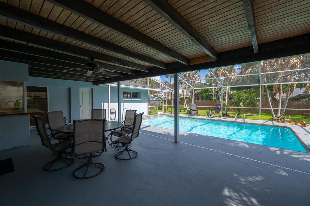 A covered patio with a dining set overlooks a screened-in swimming pool and backyard — 124 JUNE DRIVE, COCOA BEACH, FL