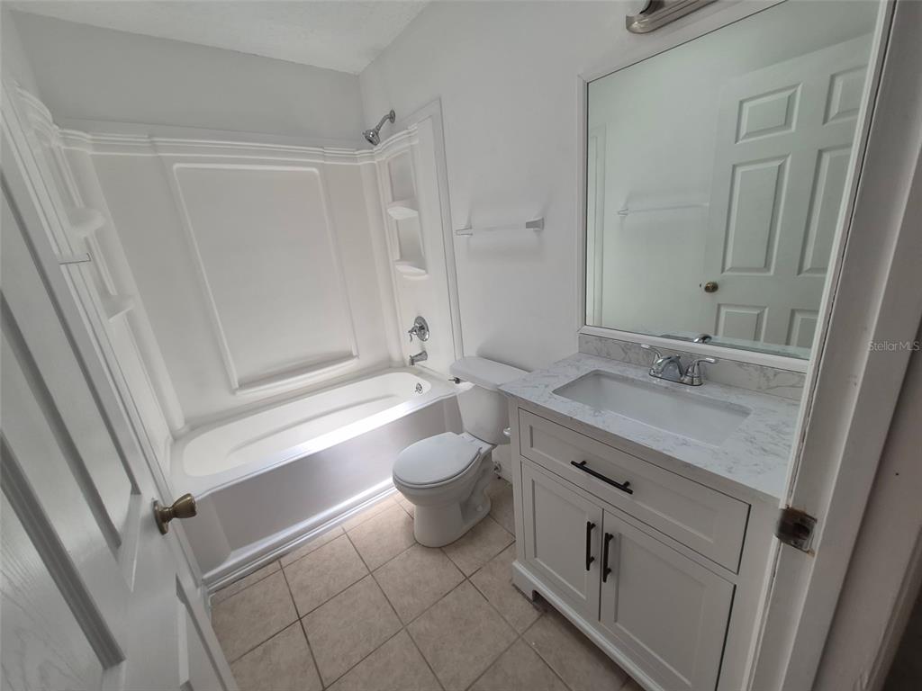 A bathroom features a white vanity with a marble countertop, a toilet, and a tub-shower — 13678 SE 55TH AVENUE, SUMMERFIELD, FL