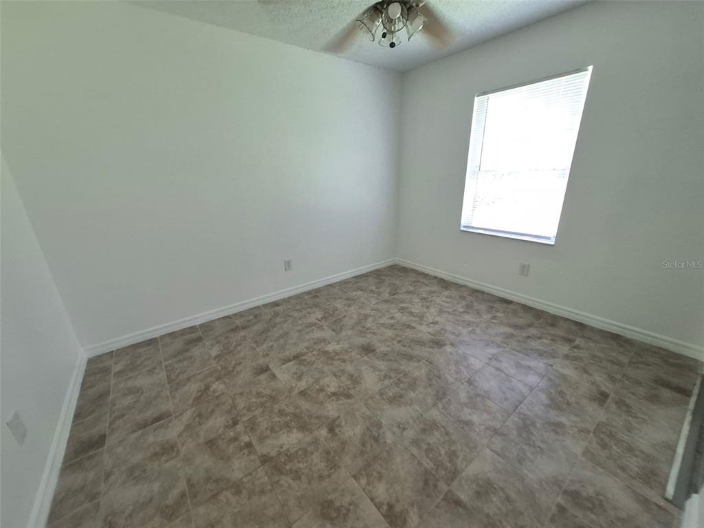An empty bedroom features white walls, a window with blinds, and light-colored tile flooring — 13678 SE 55TH AVENUE, SUMMERFIELD, FL
