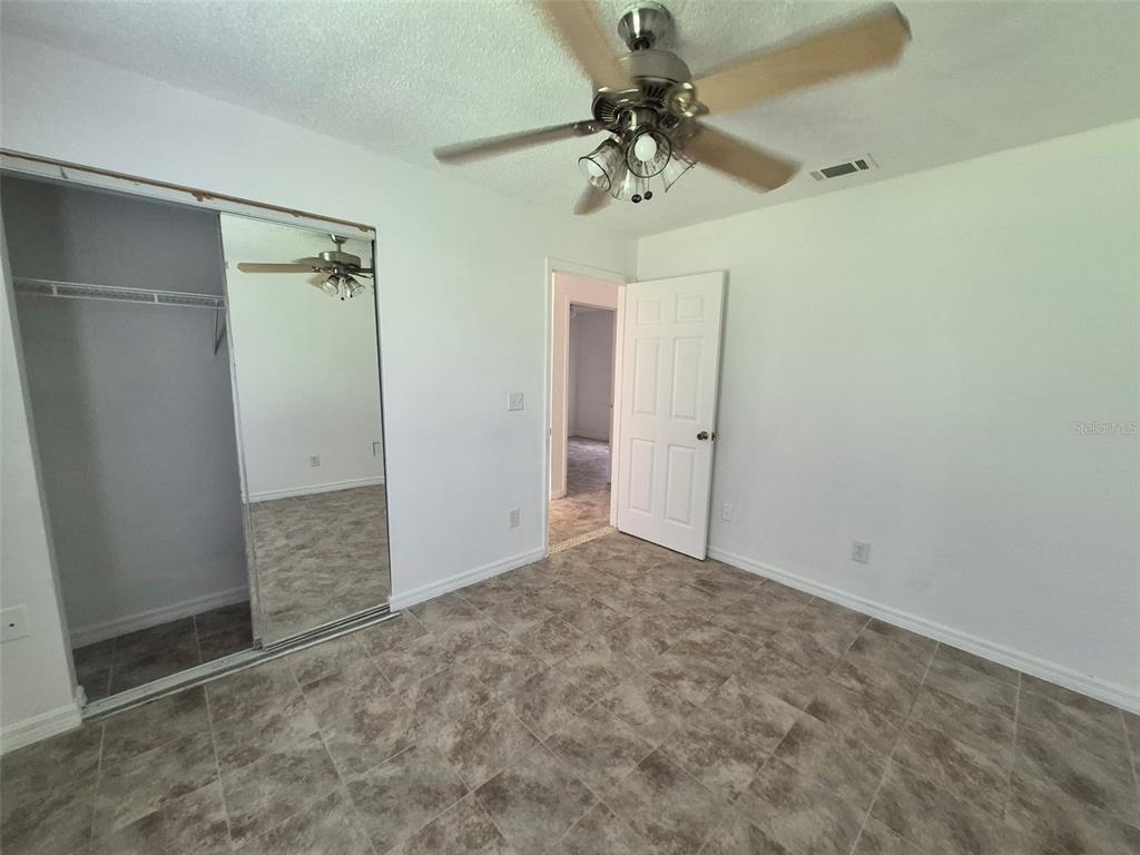 A bedroom with tiled flooring, a ceiling fan, and a mirrored sliding closet door — 13678 SE 55TH AVENUE, SUMMERFIELD, FL