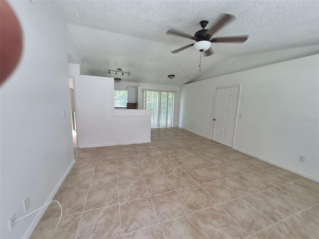 An open-concept living area features light-colored tile flooring, white walls, a ceiling fan, and sliding doors — 13678 SE 55TH AVENUE, SUMMERFIELD, FL