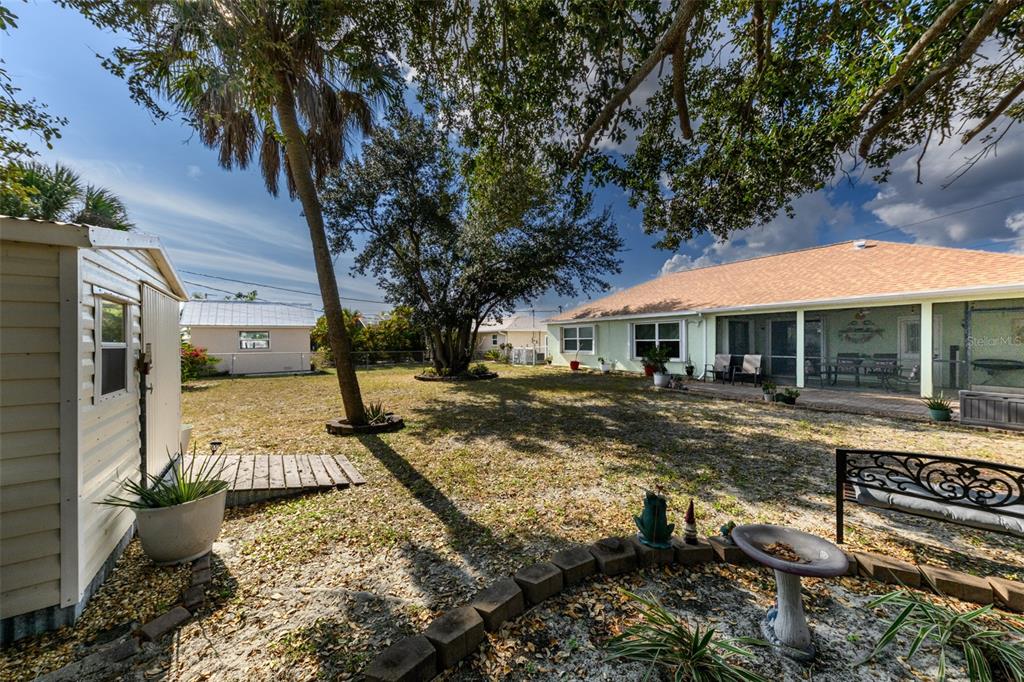 A backyard features a storage shed, a large tree, and a house with a patio — 4360 FLAMINGO BOULEVARD, PORT CHARLOTTE, FL