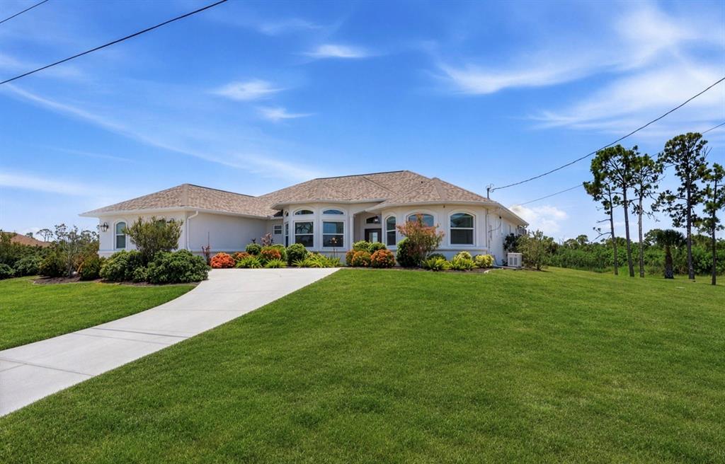 A single-story white house with a tan shingled roof sits behind a large green lawn — 1165 BOUNDARY BOULEVARD, ROTONDA WEST, FL