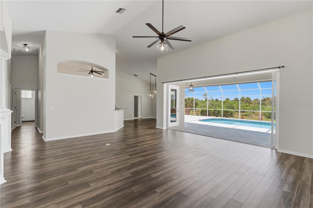 A spacious living area with wood-look flooring, a ceiling fan, and sliding doors to a pool — 1165 BOUNDARY BOULEVARD, ROTONDA WEST, FL