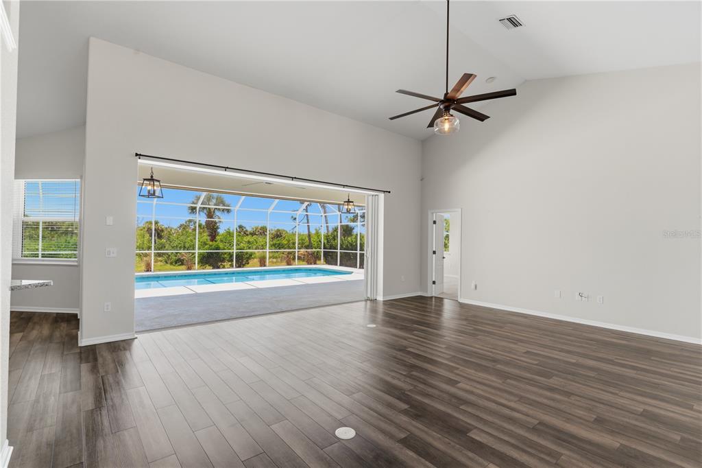 A spacious living room with wood-look flooring, a vaulted ceiling, and sliding doors opening to a pool — 1165 BOUNDARY BOULEVARD, ROTONDA WEST, FL
