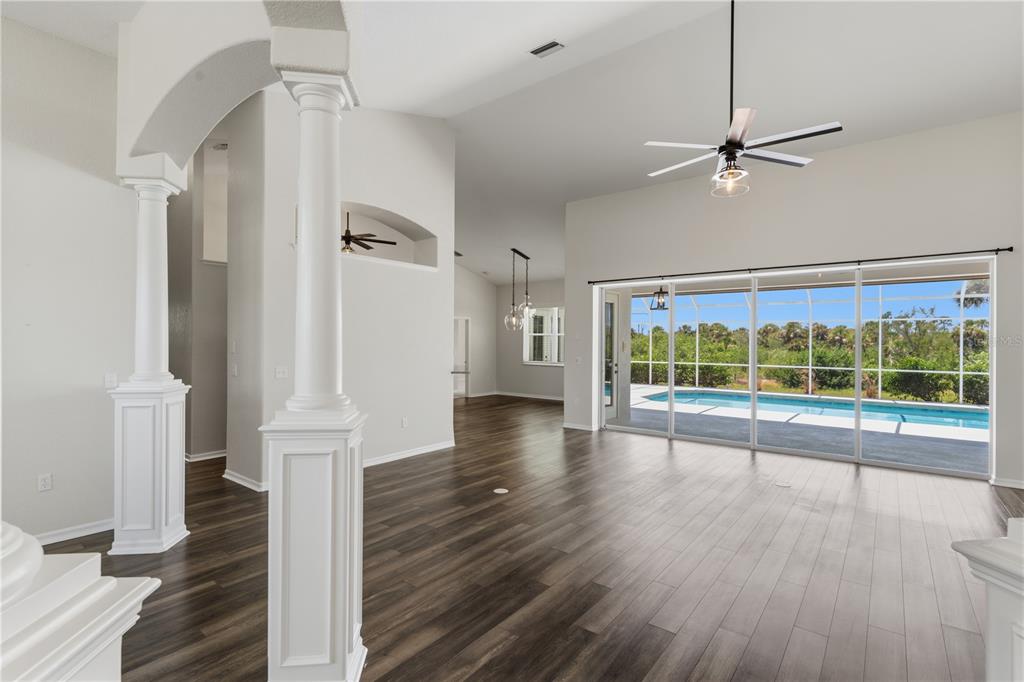 An open-concept living area with dark wood-look flooring, white columns, and sliding glass doors — 1165 BOUNDARY BOULEVARD, ROTONDA WEST, FL