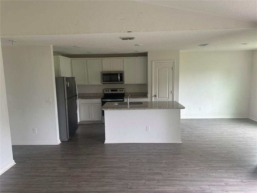 A kitchen with white cabinets, stainless steel appliances, and a granite-topped island on gray flooring — 521 BIG BLACK WAY, KISSIMMEE, FL