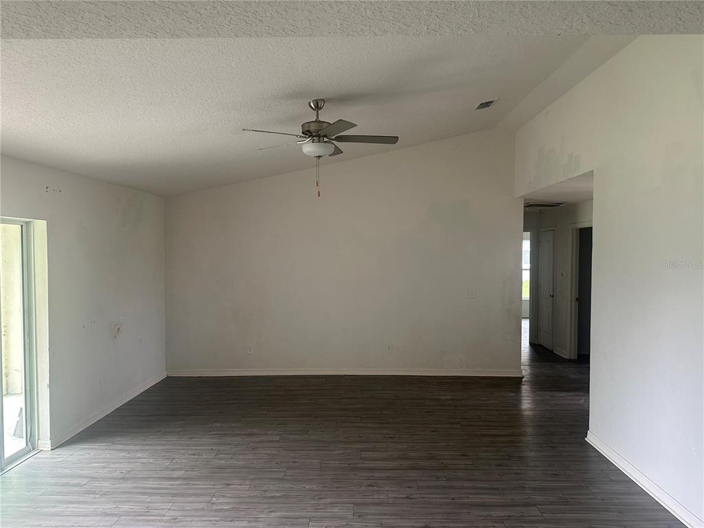 An empty living room features a vaulted ceiling, a ceiling fan, and dark wood-look flooring — 521 BIG BLACK WAY, KISSIMMEE, FL