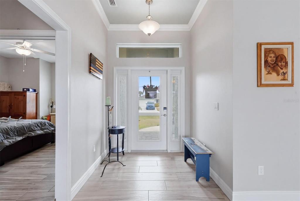 A bright entryway features light wood-look tile flooring, a white front door, and a blue bench — 48 LONG MEADOW LANE, ROTONDA WEST, FL