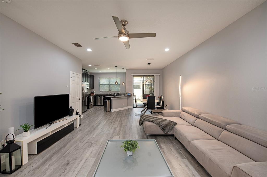 An open-concept living room and kitchen featuring light wood-look flooring and a large sectional sofa — 1990 MILKWEED, LUTZ, FL