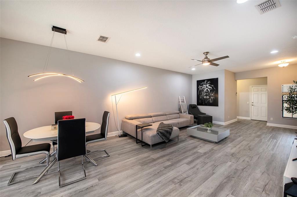 A modern open-concept living and dining area features gray wood-look flooring and a sectional sofa — 1990 MILKWEED, LUTZ, FL
