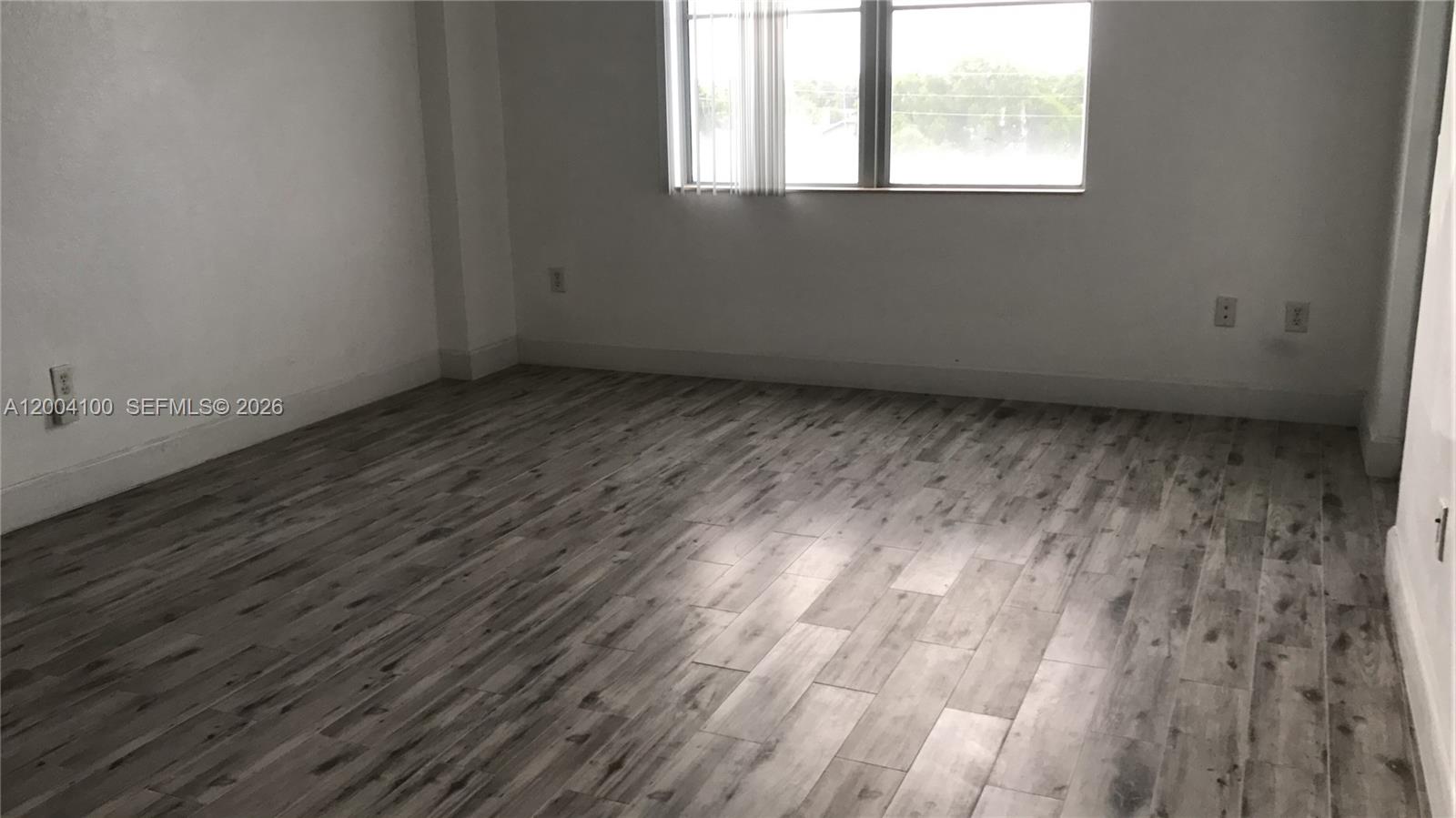 An empty room features light gray wood-look flooring, white walls, and a window with blinds — 1830 Radius Dr # 407, Hollywood FL 33020, HOLLYWOOD, FL