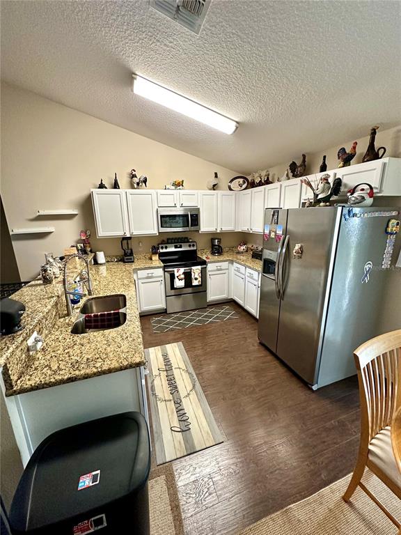 A kitchen features white cabinets, granite countertops, stainless steel appliances, and wood-look flooring — 40320 W 2ND AVENUE, UMATILLA, FL
