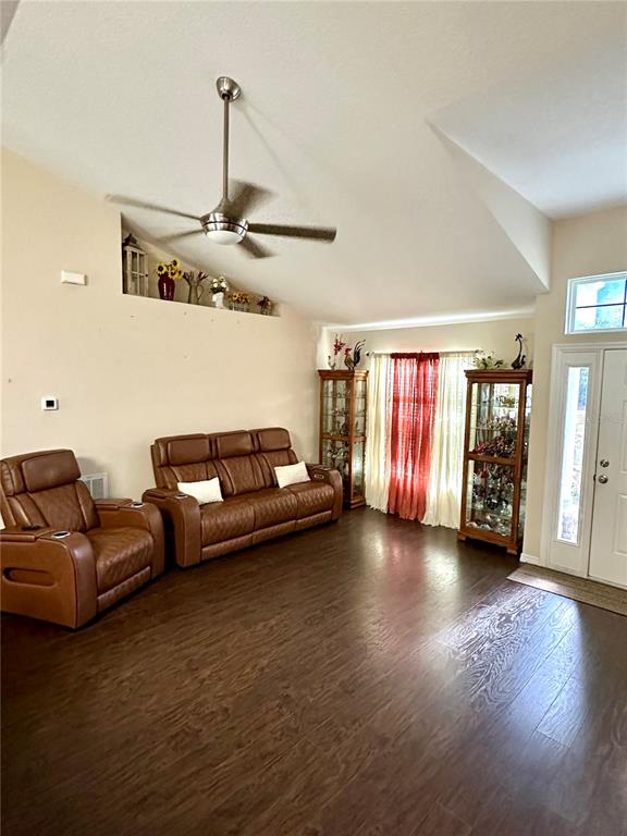 A living room features brown leather furniture, wood-look flooring, and a vaulted ceiling with a fan — 40320 W 2ND AVENUE, UMATILLA, FL