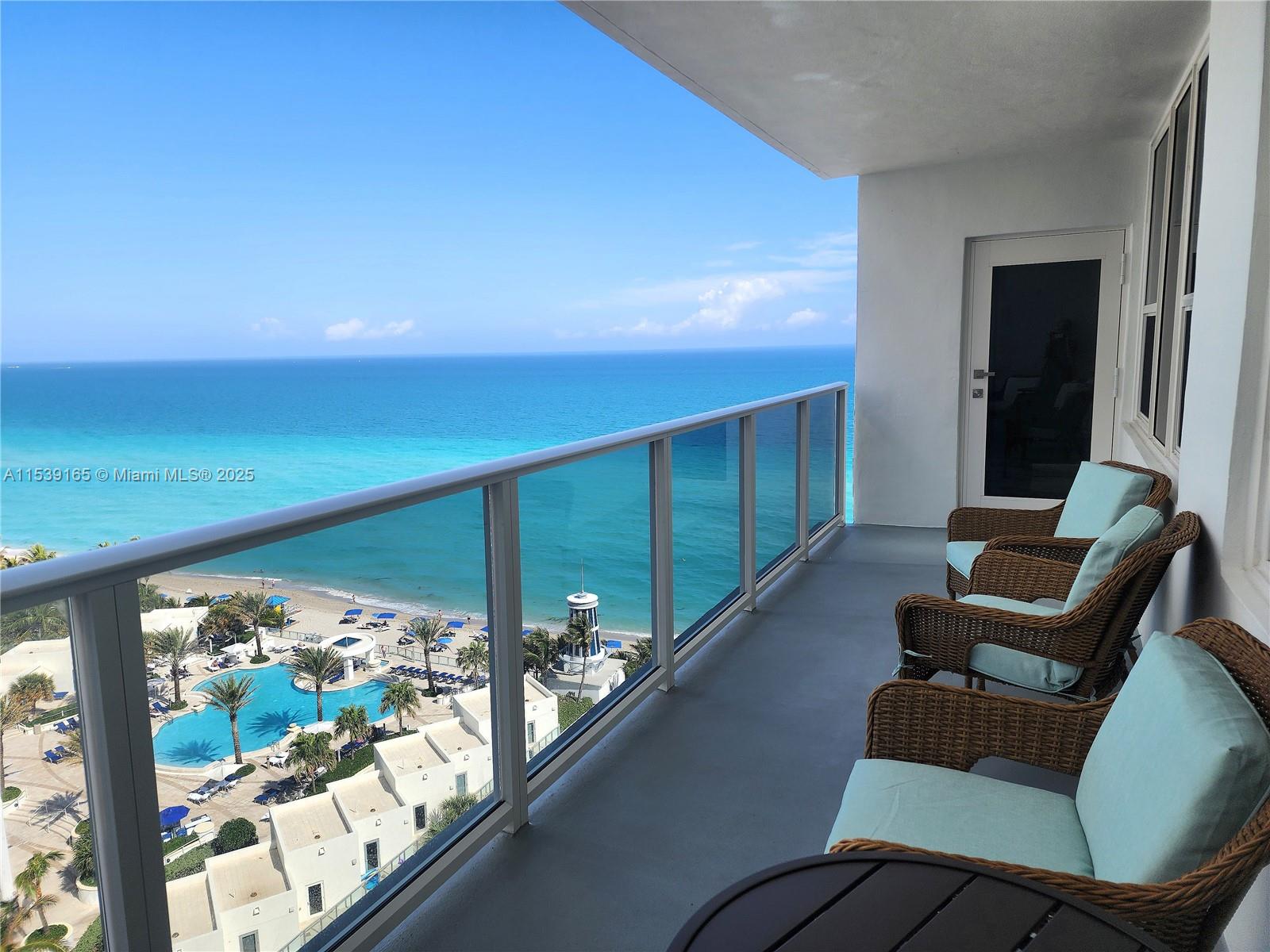 A balcony with wicker chairs overlooks a swimming pool and the ocean — 3505 S Ocean Dr # 1509, Hollywood FL 33019, HOLLYWOOD, FL