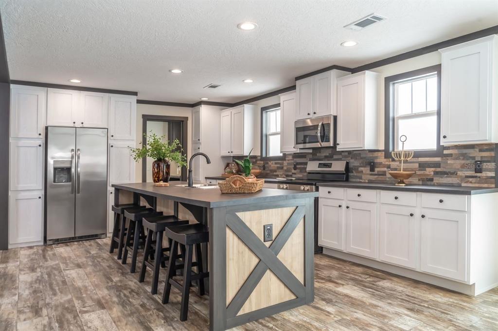 A kitchen features white cabinetry, a dark island with an X-brace, and stone tile backsplash — 10315 GREGORY AVENUE, HASTINGS, FL