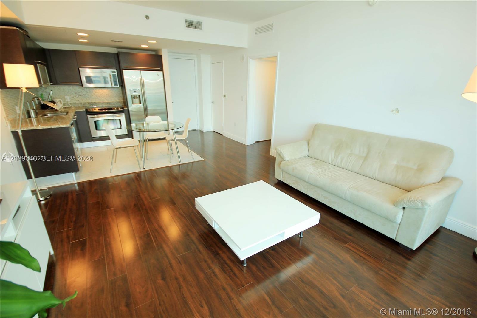 An open-concept living area features dark wood flooring, a beige sofa, and a modern kitchen — MIAMI, FL