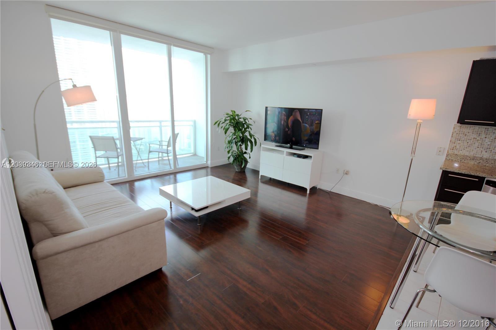 A living room features dark wood floors, a white sofa, a television, and a balcony — MIAMI, FL