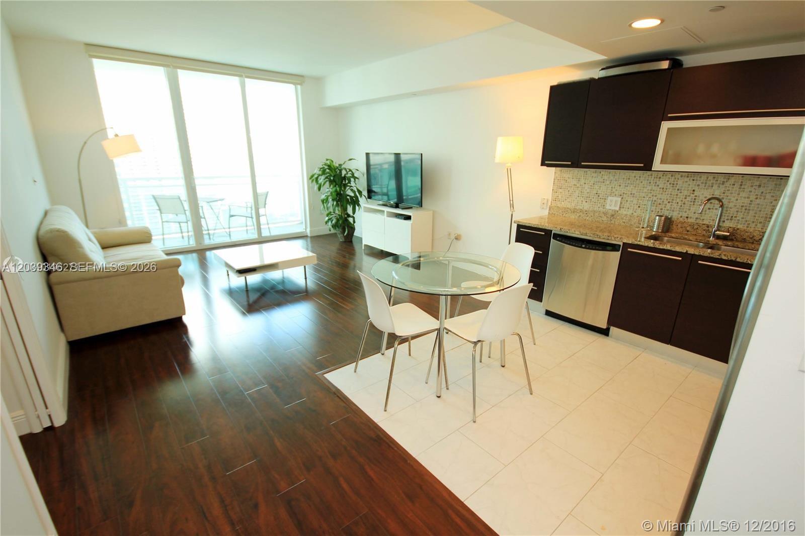 A modern apartment features an open-concept living area with dark wood floors and a kitchen — MIAMI, FL