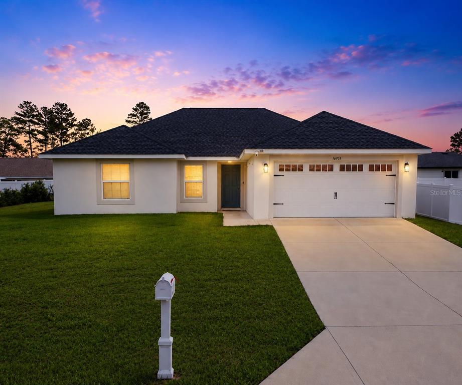 A single-story house with a white stucco exterior, a two-car garage, and a green lawn — 16951 SW 43RD COURT ROAD, OCALA, FL