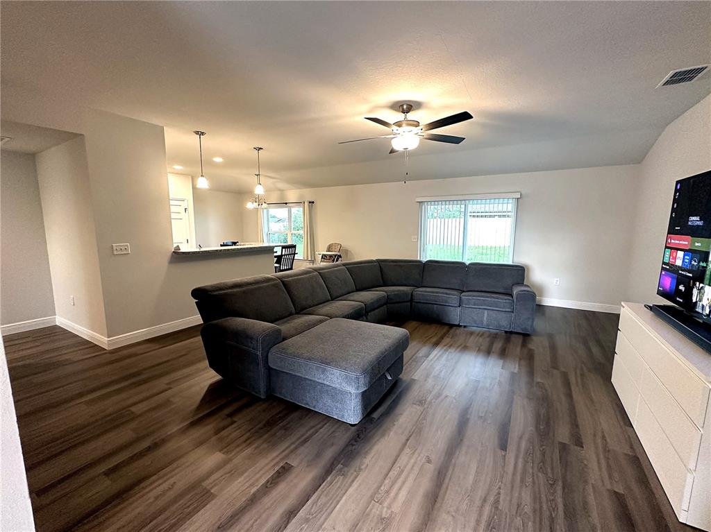 A living room with dark wood-look flooring, a large gray sectional sofa, and a television — 16951 SW 43RD COURT ROAD, OCALA, FL